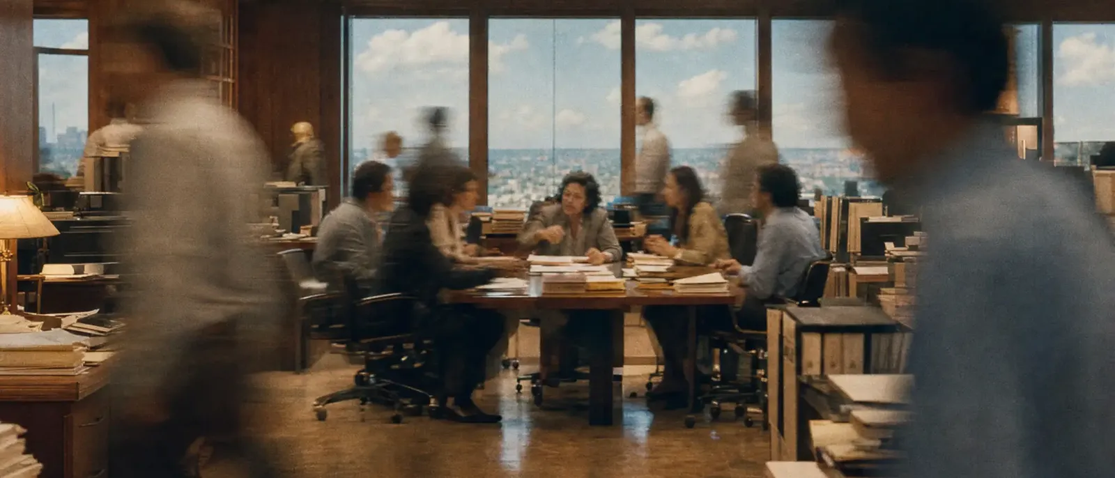 A table covered in files in an open office, people walking past in a blur